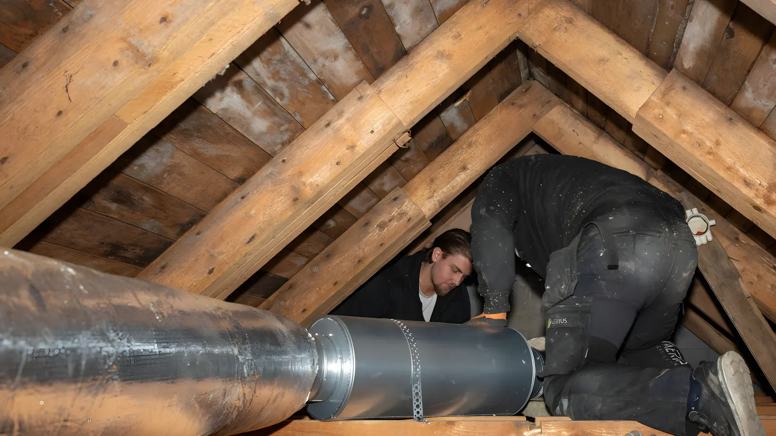 Två ventilationstekniker från Aerius arbetar med ventilationskanaler på en vind